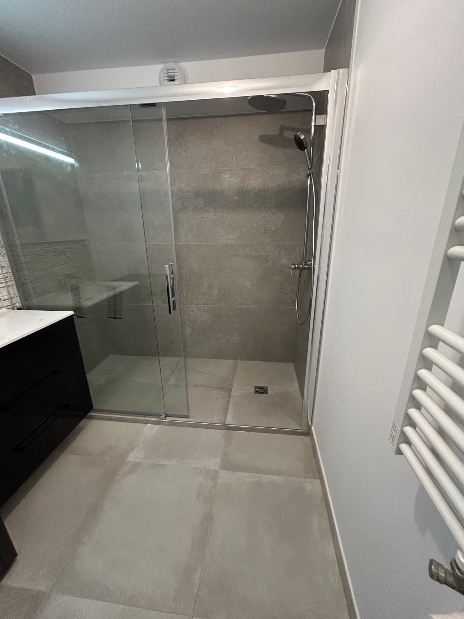 Bussy-Saint-Georges : salle d'eau avec grande douche à receveur carrelé, paroi coulissante, meuble vasque noir et sèche-serviettes